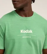Remera verde con estampa de la marca Kodak y photoprint de playa paradisíaca.