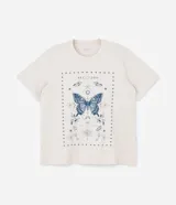 Remera color beige de corte alargado, cuello redondo y mangas cortas. Estampado frontal con una mariposa azul rodeada de elementos celestiales.