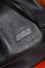 Cartera tipo botellero de cuero negro con efecto trenzado, tamaño mediano, cierre con frunce, correa ajustable con hebillas para usar al hombro o cruzada, doble bolsillo interior (uno con cierre) y forro de algodón.