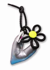 Llavero con dije de corazón plateado, flor negra con centro amarillo y etiqueta blanca con texto negro y rosa.