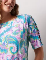 Remera estampada con diseño paisley en tonos celeste, rosa, amarillo y verde. Tiene mangas cortas con detalle de aberturas y lazos en los hombros.