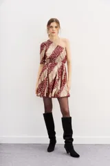 Vestido corto de un hombro, con manga larga con frunces en el hombro y ajuste con elástico en la cintura. Confeccionado en viscosa jacquard con lurex, con estampado de manchas color dorado sobre fondo borgoña.