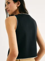 Chaleco blanco con ribete negro, cuello en V y cierre frontal con botones.