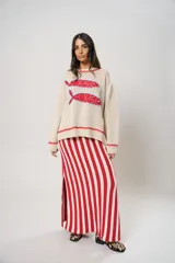 Sweater tejido color crudo con cuello redondo y mangas largas. Presenta dos peces rojos con detalles en azul bordados en el frente. Tiene ribete ondulado rojo en cuello, puños y ruedo.