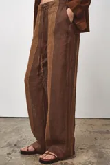 Pantalón de tiro medio confeccionado en hilatura de lino 100%. Cintura con elástico en espalda ajustable con cordones. Bolsillos laterales ocultos en costura y de plastrón en espalda.