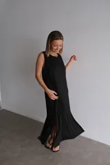 Vestido largo azul marino de tejido acanalado, con escote redondo y mangas cortas tipo hombrera. Presenta una abertura lateral en la falda.