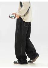 Pantalón de jean negro de corte muy ancho (baggy), con costuras exteriores en hilo blanco contrastante.