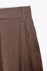 Pantalón marrón de tiro alto con trabillas, doble pliegue, bolsillos laterales y tapetas en la espalda. Pierna ancha y cierre frontal con cremallera y gancho metálico.