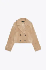 Cazadora corta estilo trench confeccionada en piel color beige. Tiene cuello solapa, manga larga con trabillas, bolsillos de vivo delanteros y cierre frontal cruzado con botones negros.