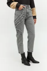 Pantalón de jean azul, estilo mom fit, con aplique fruncido en forma de espiral en la pierna izquierda.