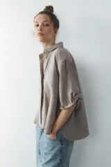Camisa azul de cuello solapa y manga corta con dobladillo. Tiene dos bolsillos de parche en el pecho, bajo asimétrico con aberturas laterales y cierre frontal con botones ocultos.