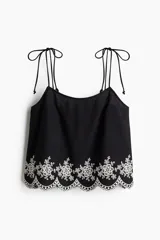 Top negro de algodón con breteles finos que se atan en moño y detalle de bordado floral blanco en el ruedo.