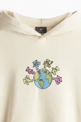 Canguro color crema de corte oversized, con capucha cruzada, hombros caídos, bolsillo tipo canguro y puños y bajo acanalados. Estampado frontal con dibujo de ositos alrededor del planeta tierra.