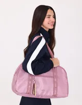 Bolso color beige de tela deportiva con manijas superiores y cierre superior. Tiene un bolsillo frontal con cierre y bolsillos laterales con cierre y tiradores de cordón y goma.