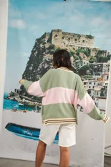 Cardigan tejido a rayas horizontales rojas y crema, con cuello redondo, cierre frontal con botones marrones y mangas largas abullonadas. Presenta ribetes a rayas en cuello, puños y ruedo. Tiene bordado el logo de la marca en el pecho.