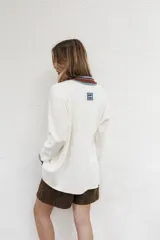 Buzo blanco de algodón con cuello polo con botones, mangas largas con puños acanalados a rayas en tonos marrón y celeste.