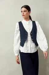 Camisa blanca con bordado floral en contraste, cuello mao, abotonadura frontal y mangas largas con frunces en los hombros.