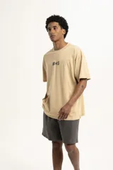 Remera color beige de corte holgado con estampado pequeño de palmera y la letra S en el centro del pecho.