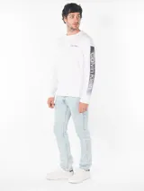 Remera blanca de algodón con cuello redondo y manga larga. Logo de Calvin Klein estampado en el pecho y diseño con letras en la manga.