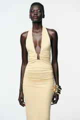 Vestido midi color crema de poliamida con cuello halter con lazada, escote pico pronunciado, detalle de pieza metálica y tejido con frunces.