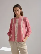 Camisa celeste de algodón con detalle de encaje blanco en el frente. Tiene mangas largas abullonadas con puños anchos y cuello redondo.