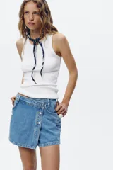 Falda pantalón de jean de tiro alto con cinco bolsillos, efecto lavado y roturas frontales. Cierre frontal con cremallera oculta y botones.