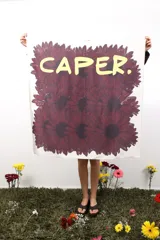 Pañuelo cuadrado de seda color crema con estampado de flores rojas y texto "CAPER." en amarillo.