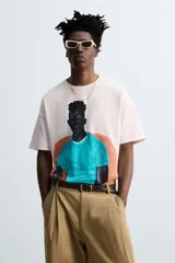 Camiseta color crema de corte holgado con cuello redondo y mangas cortas. Estampado frontal con la ilustración de un hombre sentado en un sillón.