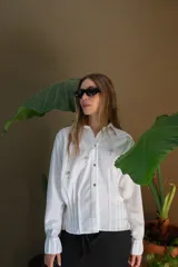 Camisa blanca de lino con bordados dorados de árboles, corte recto, cuello camisero y mangas largas con puños abotonados.