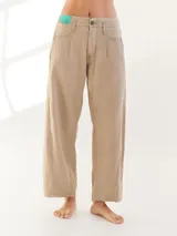 Pantalón largo color beige, tipo baggy, con costuras en verde y etiqueta turquesa en la parte trasera.