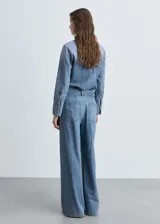 Pantalón de jean celeste de corte wide leg, tiro medio, con pinzas delanteras y cierre de cremallera y botón.