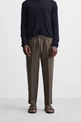 Pantalón de lino color marrón oscuro, de corte recto y relaxed fit. Tiene cintura elástica ajustable con cordón, bolsillos frontales y traseros de parche.