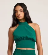 Blusa cropped marrón con escote halter, cuello alto con cierre en el cuello y pliegues en la cintura.