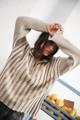 Buzo color beige con rayas horizontales en lurex dorado, cuello con medio cierre, corte oversized y logo tejido en el puño.