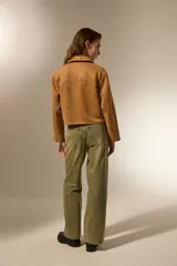 Campera cropped color camel de poliéster, con cuello camisero, cierre frontal y un bolsillo con cierre en el pecho. Está decorada con tachas plateadas distribuidas por toda la prenda.