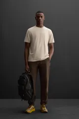 Pantalón deportivo color marrón oscuro, corte regular fit, confeccionado en tejido técnico ligero y elástico. Cuenta con cintura elástica ajustable con cordón, bolsillos frontales con cierre de cremallera, bolsillo trasero con cierre de cremallera oculta en costura y bajo ajustable con elástico.