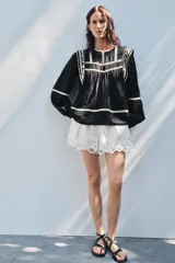 Blusa negra de algodón con cuello redondo y manga larga abullonada. Presenta bordados blancos a contraste en el cuello, hombros y mangas. Cierre en la espalda con abertura y botón.