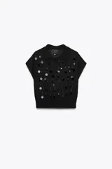 Jersey negro de punto con cuello solapa, manga corta y detalle de lentejuelas plateadas y negras.