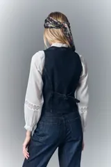 Chaleco sastrero de denim azul oscuro con elastano, acceso con botones con logo, falsos bolsillos ojal y tira de ajuste en la espalda con hebilla. Bordado de alas en la espalda.