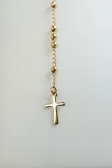 Collar tipo rosario dorado con cuentas y dije de cruz.