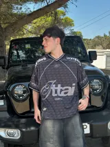 Camiseta negra con estampado de logos en gris y blanco, cuello redondo y mangas cortas. Diseño con ribetes blancos en cuello y mangas.