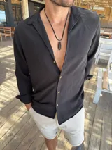 Camisa negra de fibrana, de corte clásico, con cuello camisero, manga larga con puños abotonados y cierre frontal con botones.