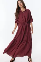Vestido camisero largo color borgoña, confeccionado en lino. Tiene cuello camisero, mangas cortas con trabilla y botón, cierre frontal con botones y cintura ajustable con cordón.
