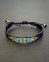 Pulsera tejida con cuentas Miyuki en tonos negro, turquesa y dorado. Ajustable con cordón negro.