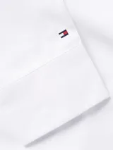 Camisa blanca de corte regular, confeccionada en popelín de algodón orgánico, con cuello inglés, puños con botón, bajo redondeado y logo de Tommy Hilfiger bordado en el pecho.