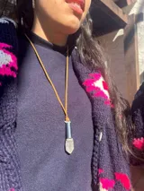 Collar con dije de cuarzo transparente facetado, engarzado en metal plateado y colgante de tiento de cuero marrón.