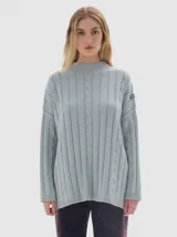 Buzo tejido de algodón color celeste, con cuello alto tipo polera, corte oversized y aberturas laterales. Presenta un diseño de punto con franjas verticales y trenzas.