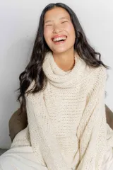 Sweater poncho color crudo de punto grueso con cuello alto y diseño holgado.