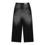 Pantalón de jean negro con lavado localizado (efecto tie-dye o acid wash), corte baggy y amplio. Presenta apliques bordados en la parte trasera de los bolsillos y herrajes metálicos cromados.