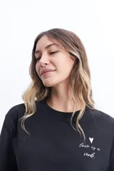 Remera corta color verde lima con estampado frontal de un corazón y la frase "love is a verb".